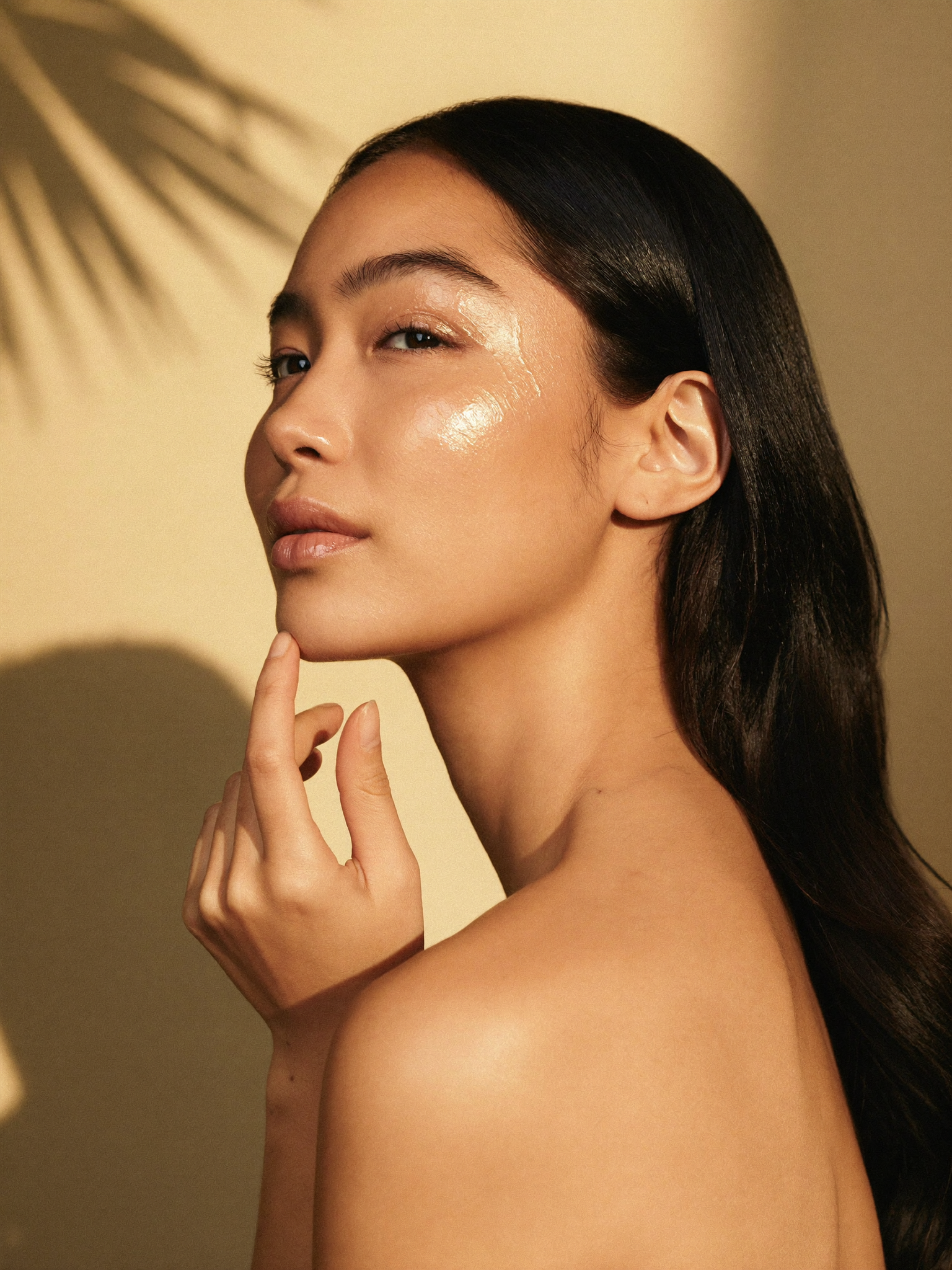 Woman with warm porcelain skin and a luminous complexion, skincare gesture