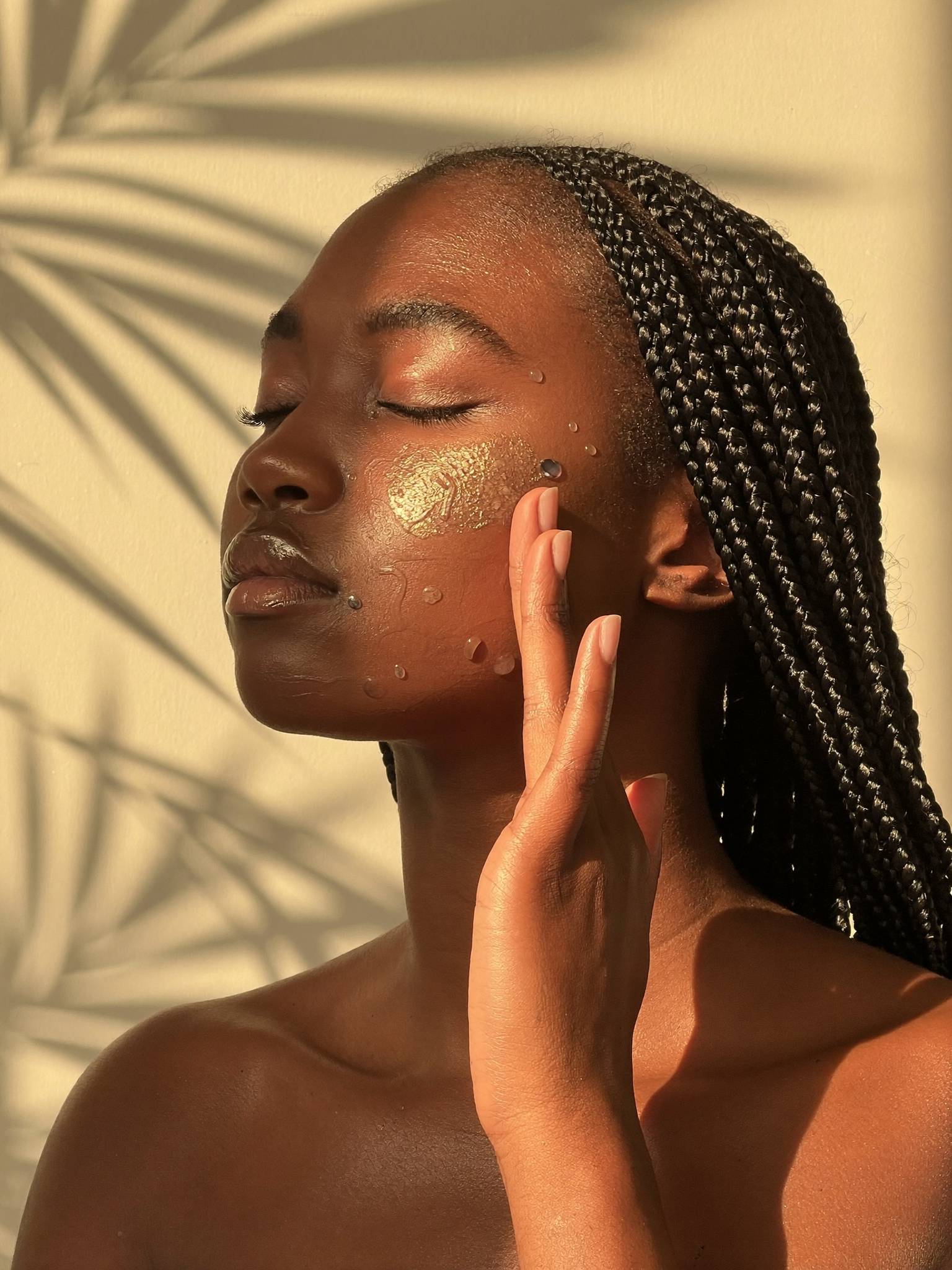 Young woman with rich melanin-rich black skin applying the Elixyrūum serum, warm light